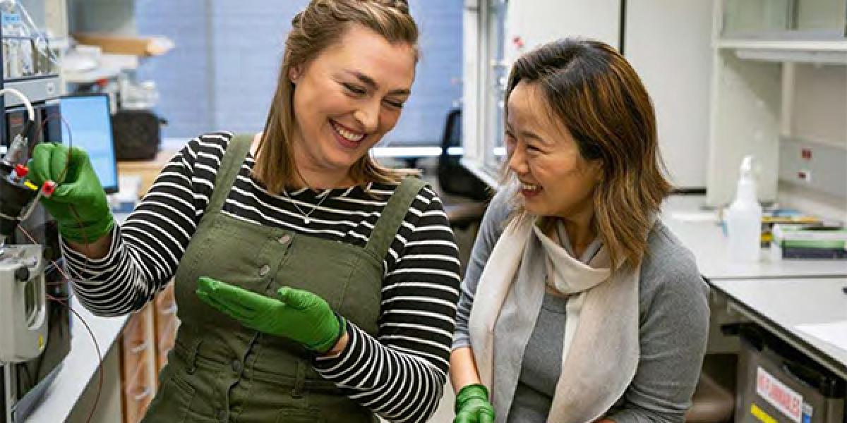 Two postdoc students smiling while in a lab working on their research